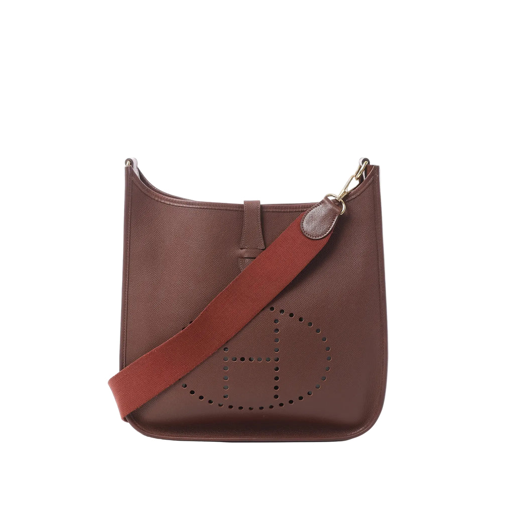 Brown leather Hermès Evelyne I 33 GM crossbody bag with perforated H logo and wide burgundy canvas strap on white background.