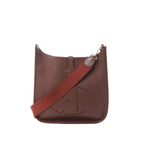 Brown leather Hermès Evelyne I 33 GM crossbody bag with perforated H logo and wide burgundy canvas strap on white background.