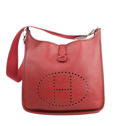 Hermès Evelyne II 33 GM shoulder bag in red Taurillon Clemence leather featuring a perforated “H” logo, flap closure, and wide red canvas strap.