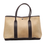 Hermès Garden Party 36 PM canvas tote with dark brown leather handles, vertical leather trim, base detailing and silver-tone snap closure.