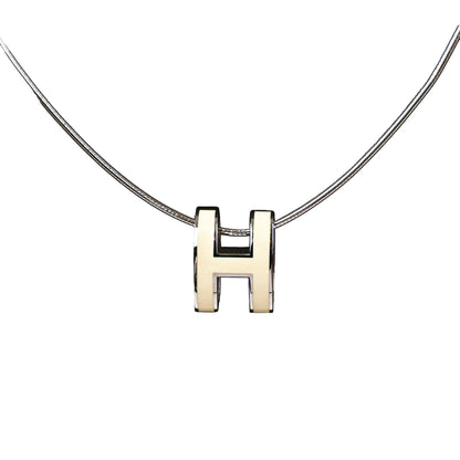 Close-up of a Hermès Pop H Necklace featuring an ecru enamel "H" pendant on a sleek silver chain, combining minimalist elegance with signature Hermès style.