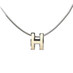 Close-up of a Hermès Pop H Necklace featuring an ecru enamel "H" pendant on a sleek silver chain, combining minimalist elegance with signature Hermès style.