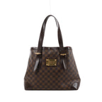 Brown Louis Vuitton Hampstead MM Damier Ebene shoulder bag with dark leather straps, reinforced corners and a gold-tone front nameplate.