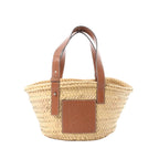 Front view of LOEWE Anagram Basket Small in beige woven raffia with brown leather shoulder straps and a brown leather Anagram logo patch.
