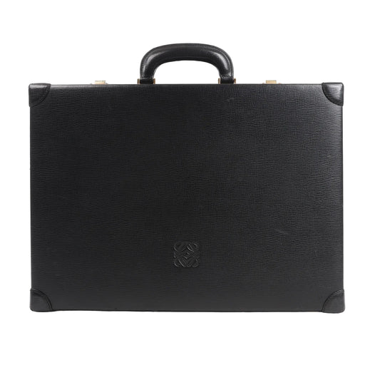 Loewe Anagram travel bag in black textured leather featuring a structured rectangular silhouette, top handle, reinforced leather corners, and embossed Anagram logo at the center, displayed against a white background.