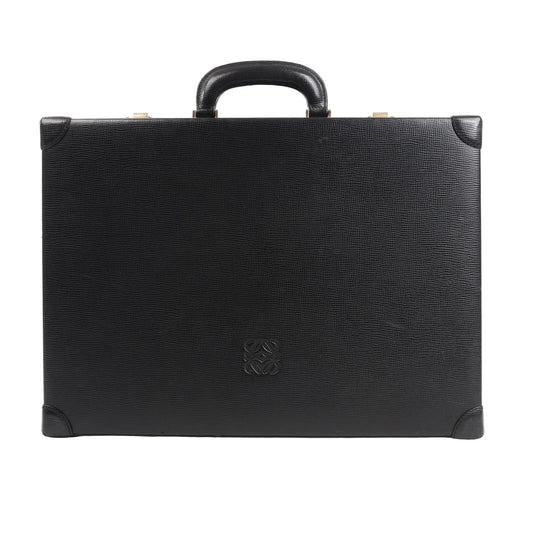 Loewe Anagram travel bag in black textured leather featuring a structured rectangular silhouette, top handle, reinforced leather corners, and embossed Anagram logo at the center, displayed against a white background.