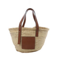 LOEWE Basket Large handbag in beige woven raffia with brown leather shoulder straps, embossed leather logo patch, and open-top tote shape on white background.