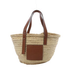 LOEWE Basket Large handbag in beige woven raffia with brown leather shoulder straps, embossed leather logo patch, and open-top tote shape on white background.