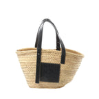 LOEWE Medium Basket bag in beige woven raffia with black leather shoulder straps and a black leather LOEWE logo patch on the front.
