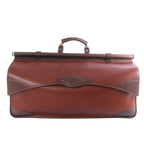 Brown Loewe leather travel bag with elongated structured body, darker brown trim, top handle and metal hardware on a white background.