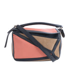 Small Loewe Puzzle bag in black, coral pink and tan leather with geometric panels, a top handle and detachable shoulder strap.