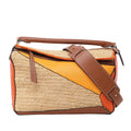 Front view of LOEWE Puzzle Medium Raffa and Leather 2Way Handbag in orange, brown, and beige, featuring geometric panel design with woven raffia sections, smooth leather accents, top handle, and wide adjustable shoulder strap against a white background.