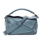 Front view of LOEWE Puzzle Medium Leather 2Way Handbag in blue, showcasing geometric panel design, smooth leather finish, top handle, wide adjustable shoulder strap, and subtle embossed logo on top corner against a white background.