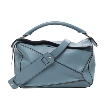 Front view of LOEWE Puzzle Medium Leather 2Way Handbag in blue, showcasing geometric panel design, smooth leather finish, top handle, wide adjustable shoulder strap, and subtle embossed logo on top corner against a white background.