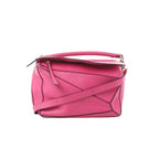 LOEWE Puzzle Medium handbag in bright pink leather with geometric panel construction, top handle, zip-top closure, and detachable shoulder strap on a white background.