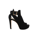 Side view of a Louis Vuitton black suede sandal with an open toe, raised platform, slender high heel and wide ankle strap with a gold-tone square buckle.