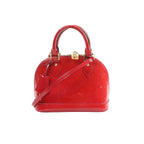 Red glossy Louis Vuitton Alma BB Monogram Vernis handbag with top handles, detachable shoulder strap, gold-tone padlock, and hanging luggage tag on a white background.