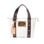Front view of a white Louis Vuitton Antigua Cabas PM canvas tote with dark brown handles, gold-tone logo plaque and tan leather luggage tag.
