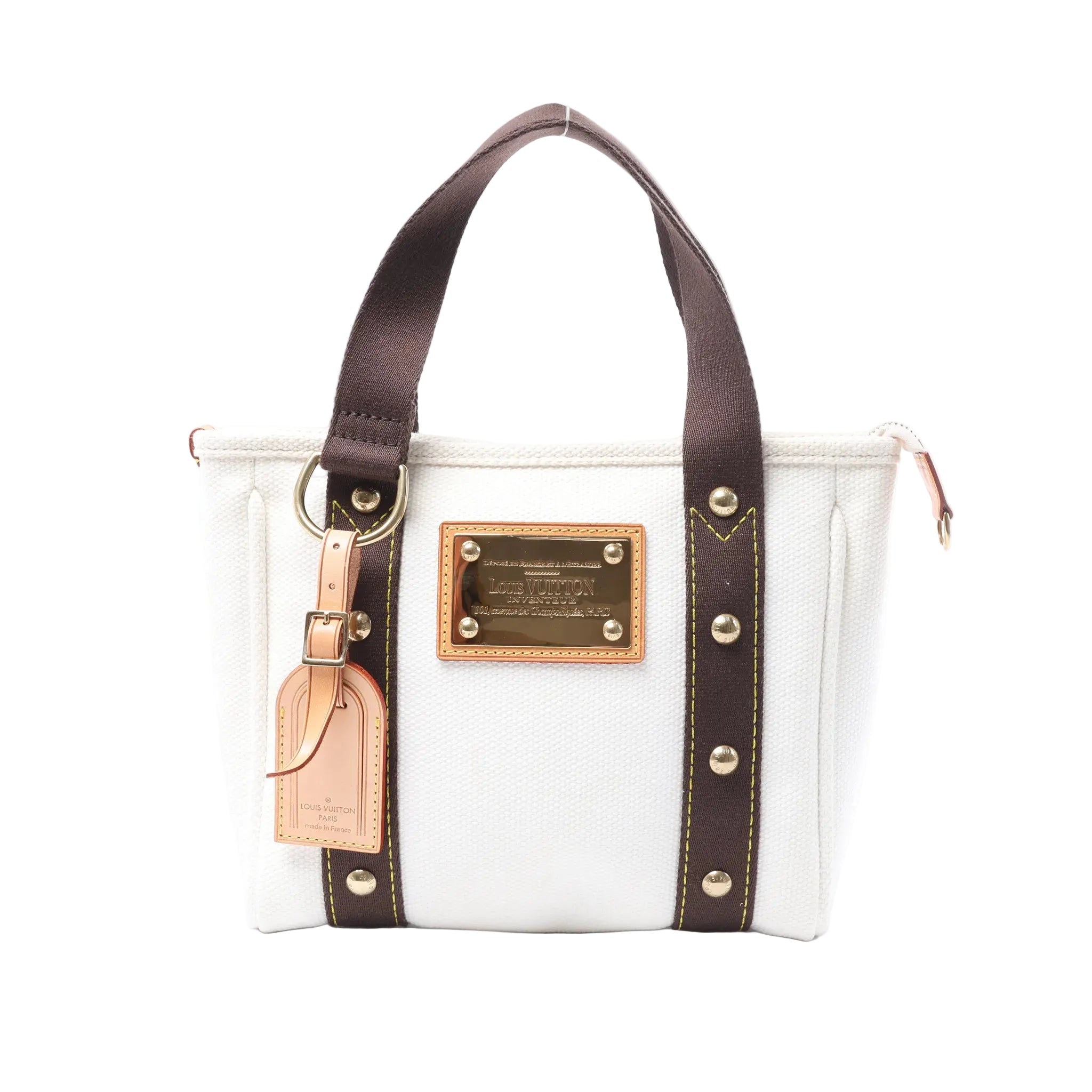 Front view of a white Louis Vuitton Antigua Cabas PM canvas tote with dark brown handles, gold-tone logo plaque and tan leather luggage tag.