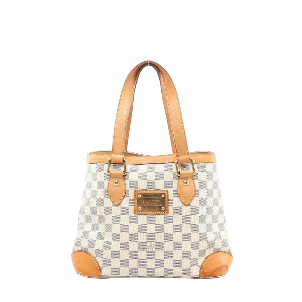 Louis Vuitton Hampstead PM Damier Azur tote handbag in beige and light blue checkered canvas with vachetta leather shoulder straps, leather corner trims, and a gold-tone front logo plaque, shown on a white background.