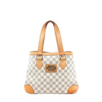 Louis Vuitton Hampstead PM Damier Azur tote handbag in beige and light blue checkered canvas with vachetta leather shoulder straps, leather corner trims, and a gold-tone front logo plaque, shown on a white background.