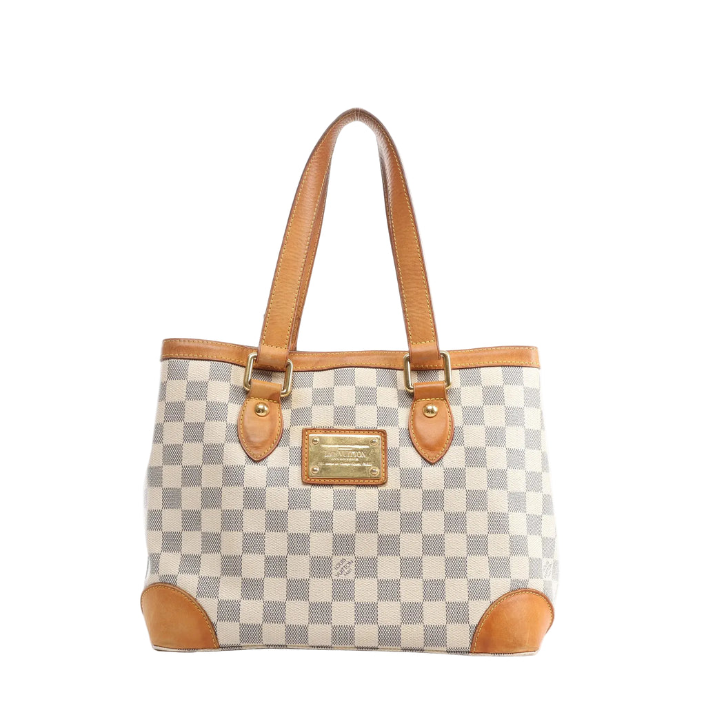Louis Vuitton Hampstead PM Damier Azur tote handbag in beige and light blue checkered canvas with vachetta leather shoulder straps, leather corner trims, and a gold-tone front logo plaque, shown on a white background.