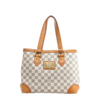 Louis Vuitton Hampstead PM Damier Azur tote handbag in beige and light blue checkered canvas with vachetta leather shoulder straps, leather corner trims, and a gold-tone front logo plaque, shown on a white background.