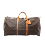 Louis Vuitton Keepall 60 brown Monogram canvas travel duffle with vachetta leather top handles, two vachetta leather bands, hanging leather tag, and top zip closure, shown on a white background.
