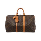 A brown Louis Vuitton Keepall Bandoulière 45 travel bag in Monogram coated canvas, featuring tan leather top handles, central leather trim, and an attached luggage tag.