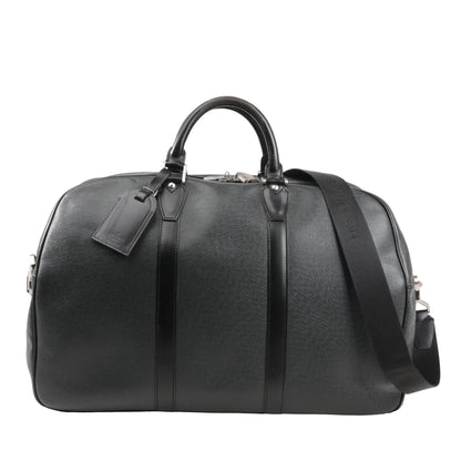 Front view of a Louis Vuitton Kendall PM M30122 travel bag in black Taiga leather featuring structured dual top handles, a detachable black shoulder strap, silver-tone hardware, and matching leather luggage tag.