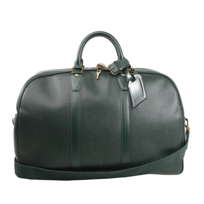 Louis Vuitton Kendall PM travel bag in deep green Taiga leather, featuring structured top handles, detachable shoulder strap, gold-tone hardware, and luggage tag detail.