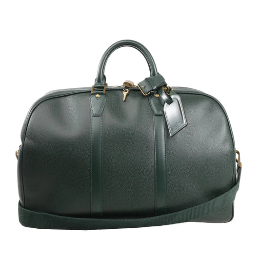 Louis Vuitton Kendall PM travel bag in deep green Taiga leather, featuring structured top handles, detachable shoulder strap, gold-tone hardware, and luggage tag detail.