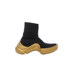 Side view of a Louis Vuitton black knit high-top sock sneaker with a ribbed cuff, tonal lettering and an oversized wave-shaped gold sole.
