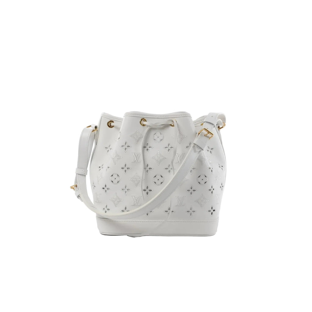 White Louis Vuitton Petit Noé NM bucket bag with Monogram cutout pattern, drawstring closure, gold-tone grommets, and adjustable shoulder strap.
