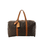 Louis Vuitton Sac Souple 45 brown Monogram canvas travel bag with vachetta leather trim, long top handles, and luggage tag on white background.