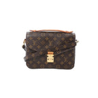 Front view of Louis Vuitton Monogram canvas Pochette Métis MM with tan leather top handle, gold-tone S-lock clasp, and crossbody strap on white background.