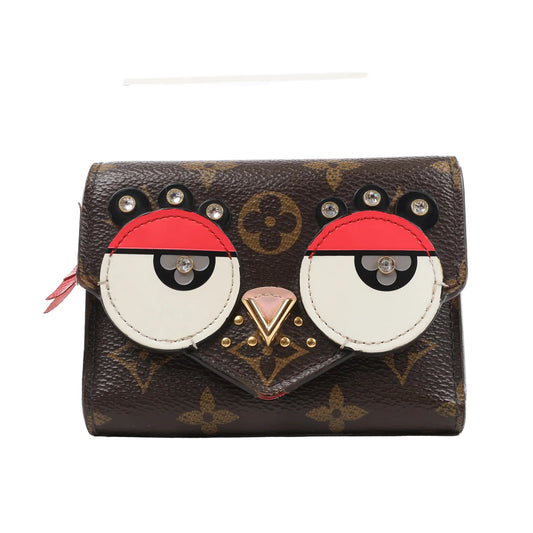 Front view of the Louis Vuitton Monogram Portefeuille Victorine Lovely Bird wallet (M67244), featuring brown monogram canvas with red, white, and black leather appliqués forming a bird face, accented with gold-tone studs and rhinestone eyes.