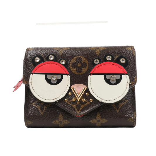 Front view of the Louis Vuitton Monogram Portefeuille Victorine Lovely Bird wallet (M67244), featuring brown monogram canvas with red, white, and black leather appliqués forming a bird face, accented with gold-tone studs and rhinestone eyes.