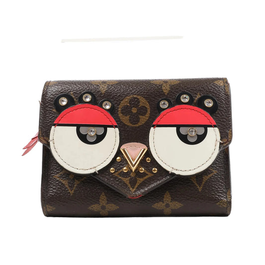 Front view of the Louis Vuitton Monogram Portefeuille Victorine Lovely Bird wallet (M67244), featuring brown monogram canvas with red, white, and black leather appliqués forming a bird face, accented with gold-tone studs and rhinestone eyes.