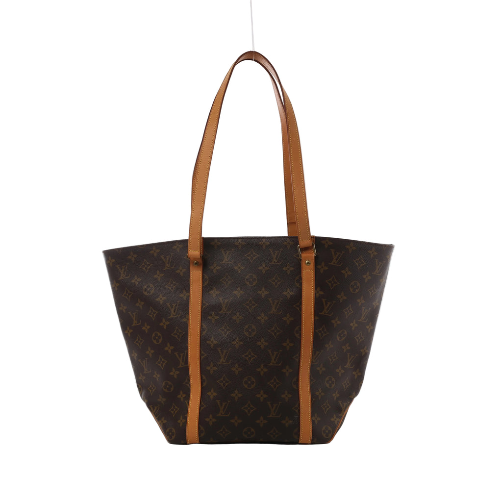 Brown Louis Vuitton Sac Shopping Monogram canvas tote with long tan leather shoulder straps and vertical leather trim, shown front-on against white.