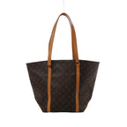 Brown Louis Vuitton Sac Shopping Monogram canvas tote with long tan leather shoulder straps and vertical leather trim, shown front-on against white.
