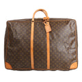 Louis Vuitton Sirius 65 travel bag in brown Monogram Canvas featuring natural Vachetta leather top handles, vertical leather trim, gold-tone hardware, and a large rectangular silhouette with rounded corners and luggage tag detail.
