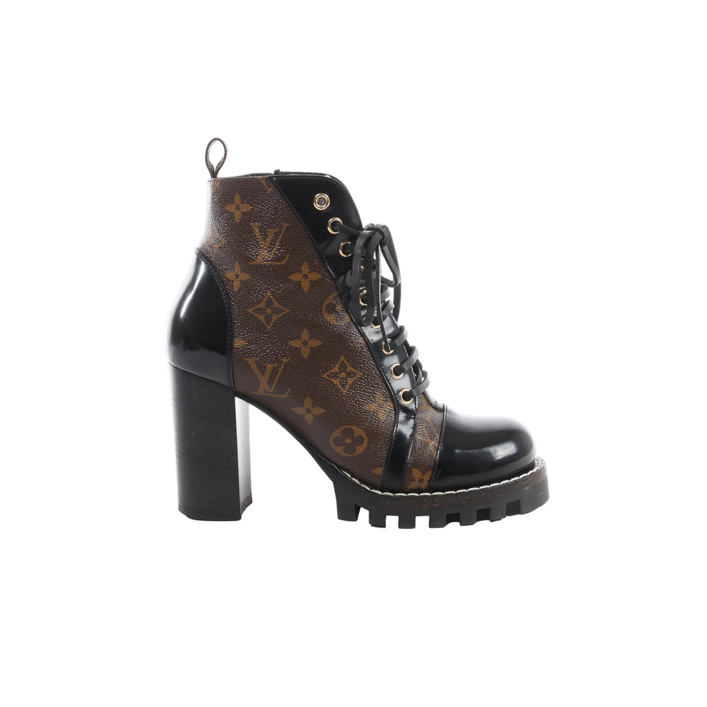Side view of a Louis Vuitton Star Trail ankle boot with brown Monogram panels, glossy black trim, black laces, gold-tone eyelets and a tall block heel.