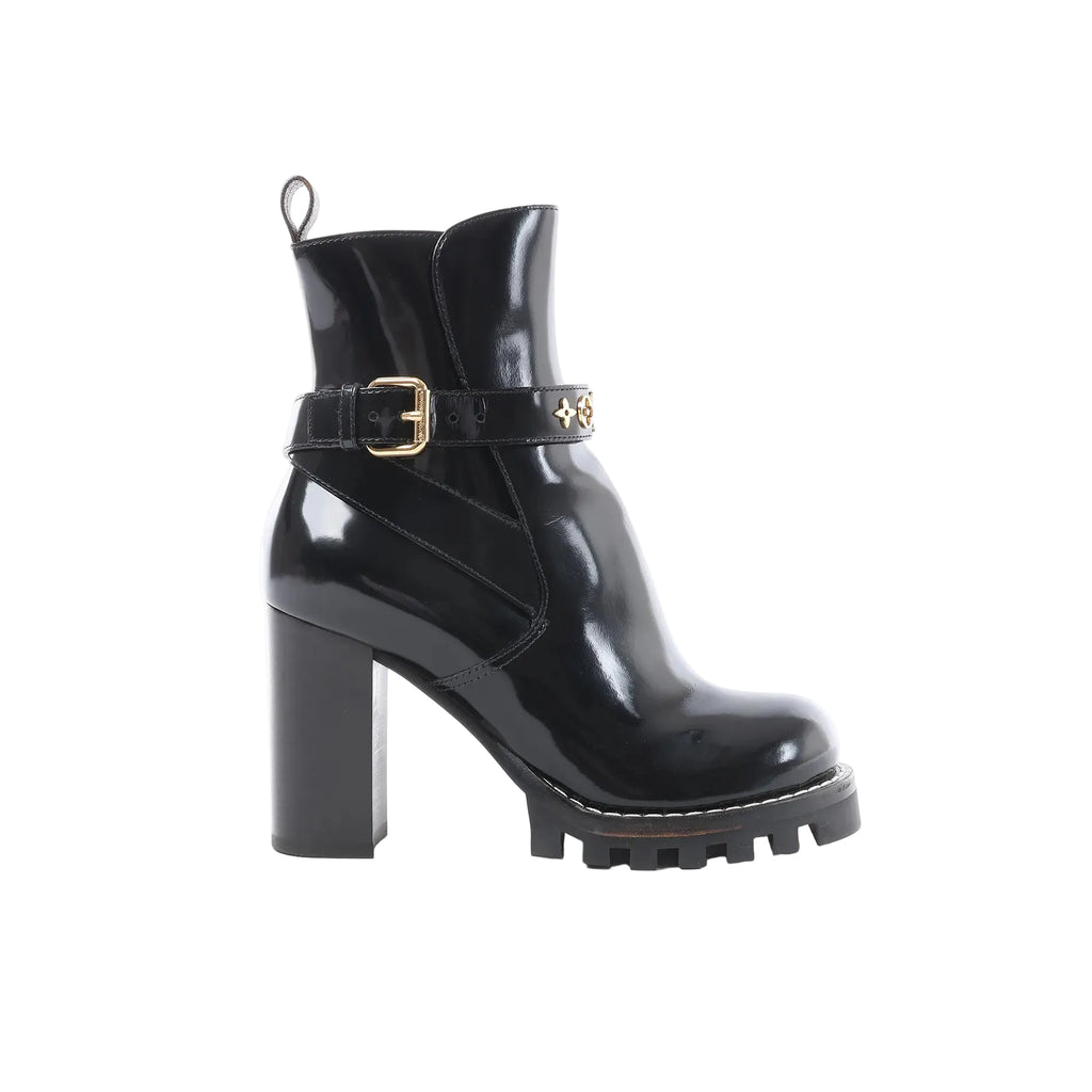 Black Louis Vuitton Star Trail Line patent leather ankle boot with gold buckle strap and monogram hardware, high block heel, and chunky lug platform sole, side view on white background