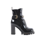 Black Louis Vuitton Star Trail Line patent leather ankle boot with gold buckle strap and monogram hardware, high block heel, and chunky lug platform sole, side view on white background