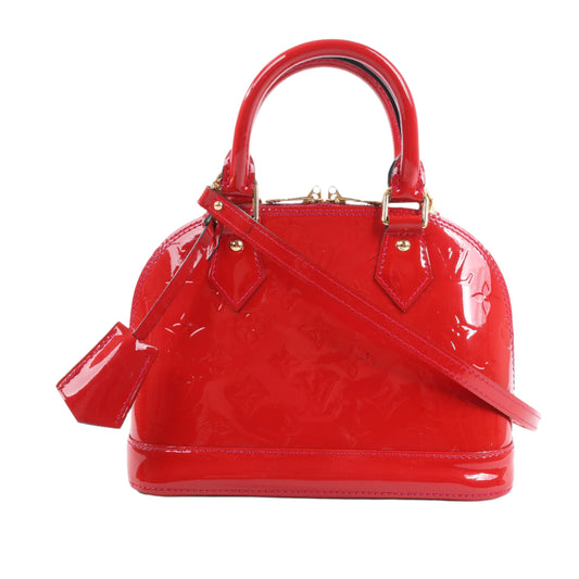 Red patent leather handbag with gold accents on a white background