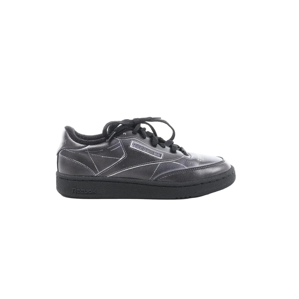 Maison Margiela x Reebok Club C black leather sneaker with black laces, stitched panel design, Reebok side logo, and black rubber sole, side view on white background