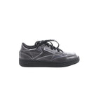 Maison Margiela x Reebok Club C black leather sneaker with black laces, stitched panel design, Reebok side logo, and black rubber sole, side view on white background