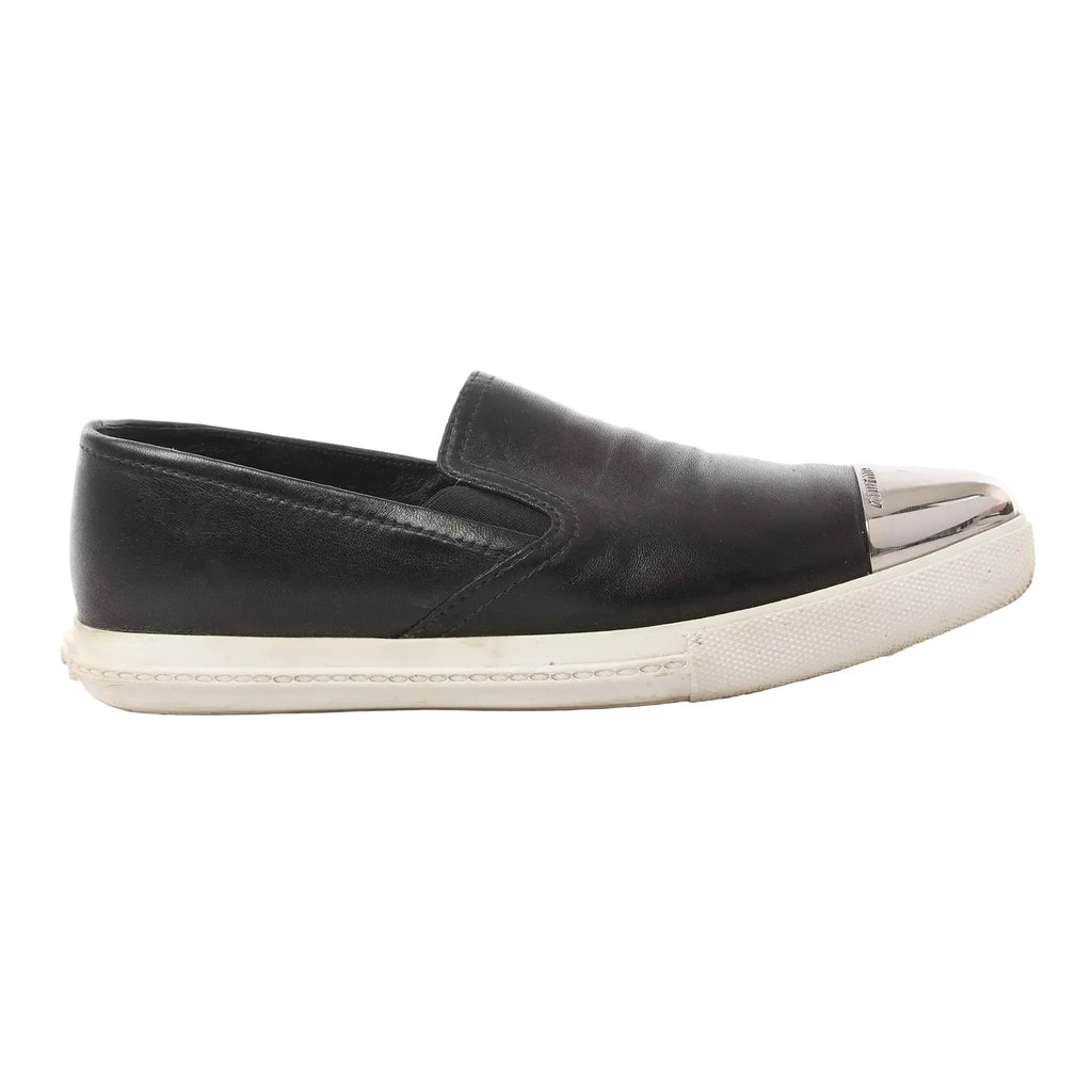 Black leather Miu Miu slip-on sneaker with silver-tone metal cap toe, elastic side gusset, and white rubber sole, shown in side view.