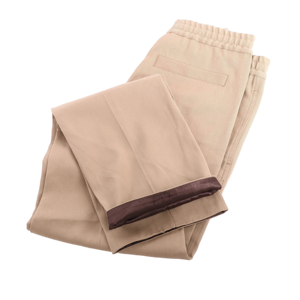 OAMC beige straight-leg trousers with elasticated waistband and back welt pocket, folded flat on white background.